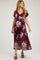 woman wearing a burgundy floral wrap maternity dress with flutter sleeves and a high-low hem, showcasing her baby bump