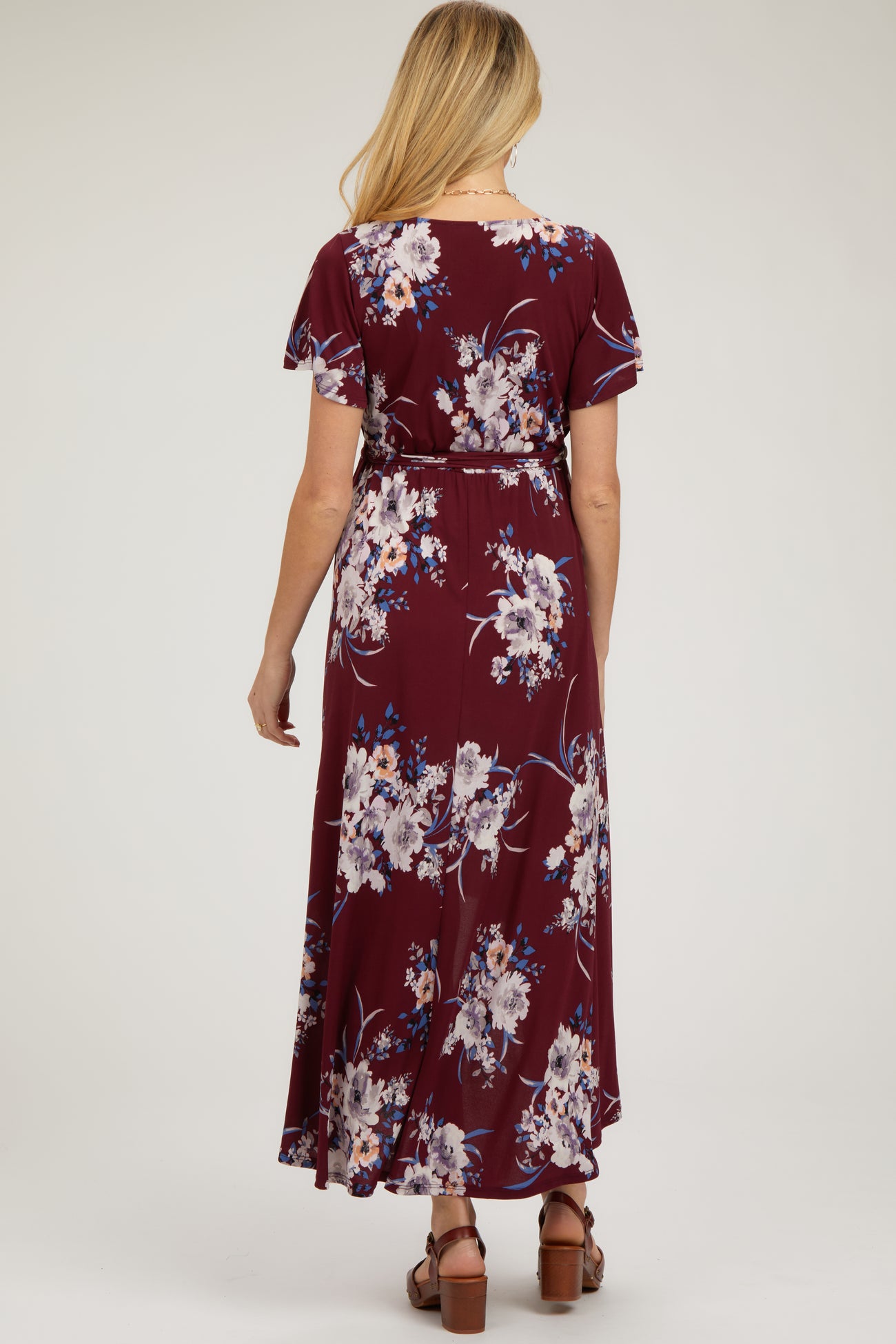 woman wearing a maroon floral maternity maxi dress with short sleeves and a tie waist from the back