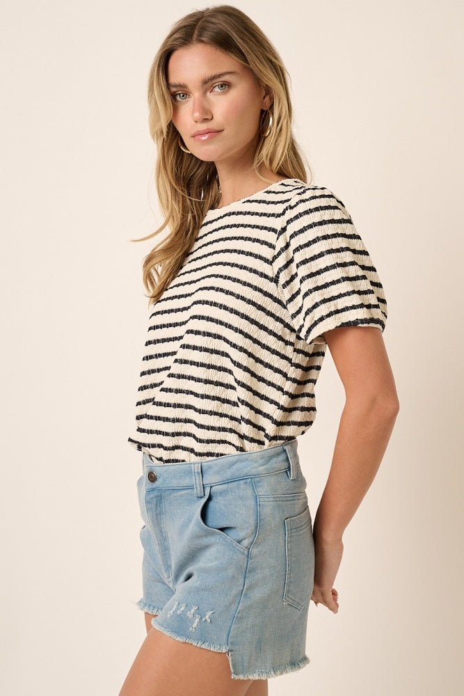 woman wearing a cream and navy striped short sleeve top with a relaxed fit and light blue denim cut-off shorts
