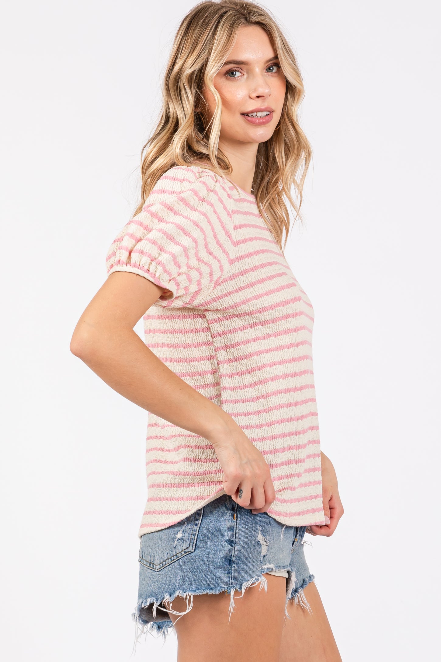 woman wearing a pink and white striped short sleeve top with smocked details and distressed denim shorts