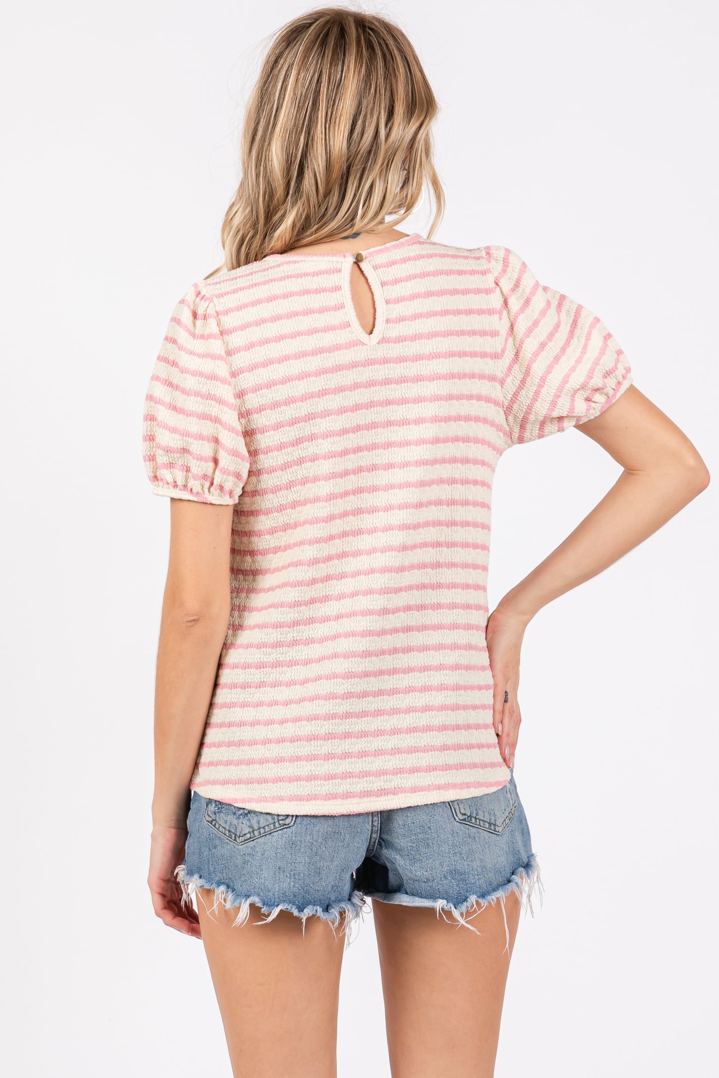 woman wearing a pink and white striped short sleeve top with a back keyhole detail and denim shorts
