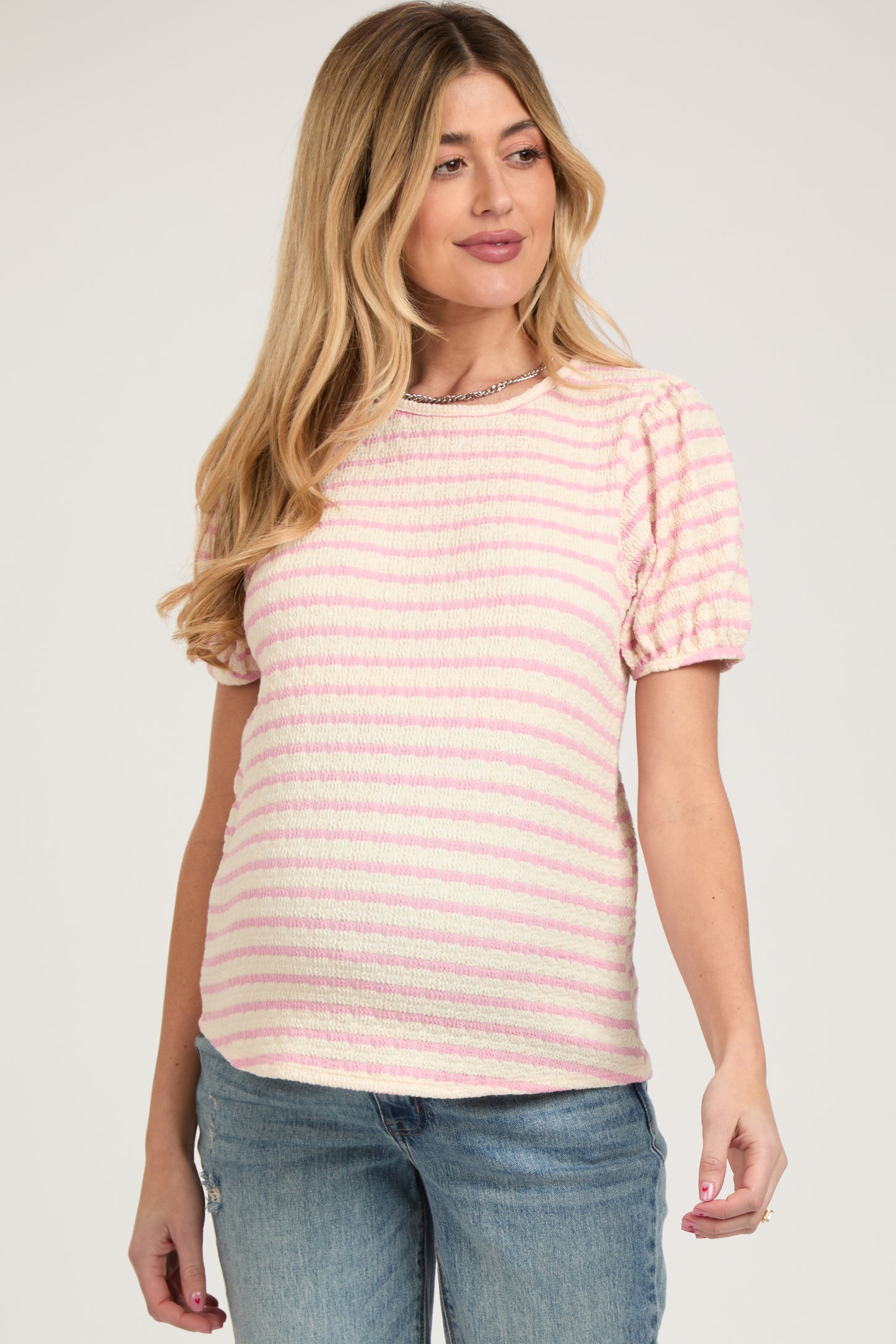 woman wearing a pink and white striped maternity top with puff sleeves, showcasing her baby bump
