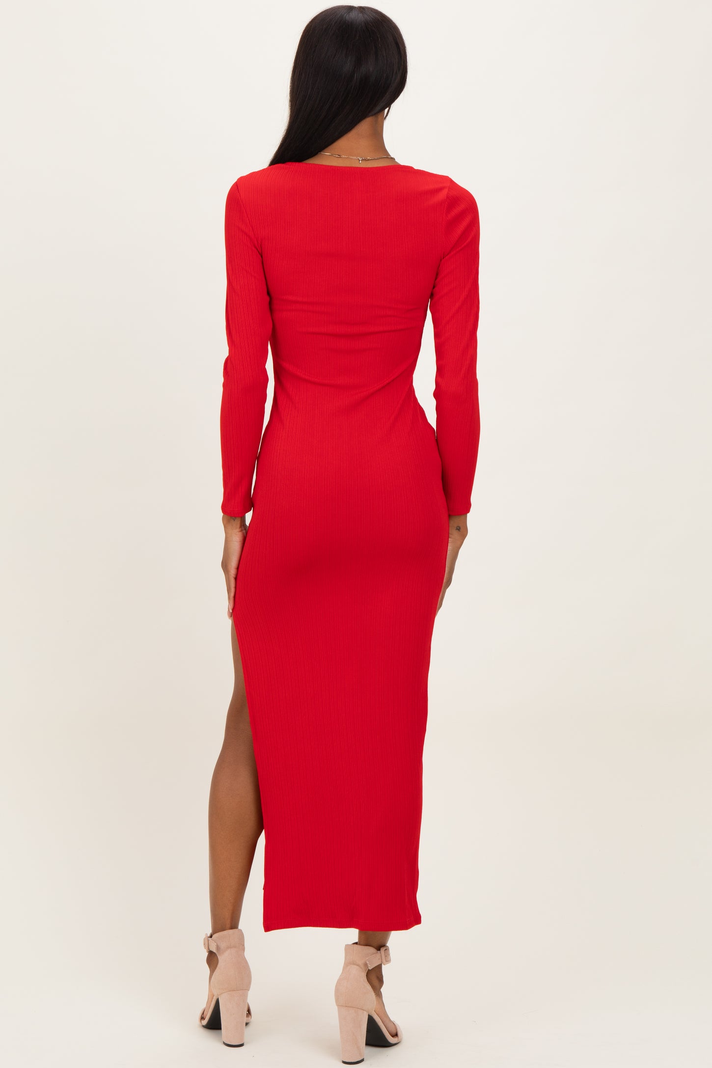 woman wearing a red ribbed long sleeve maxi dress with a side slit and strappy heels, shown from the back