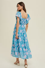 woman wearing a blue floral maxi dress with puff sleeves and a smocked bodice, standing with her back to the camera