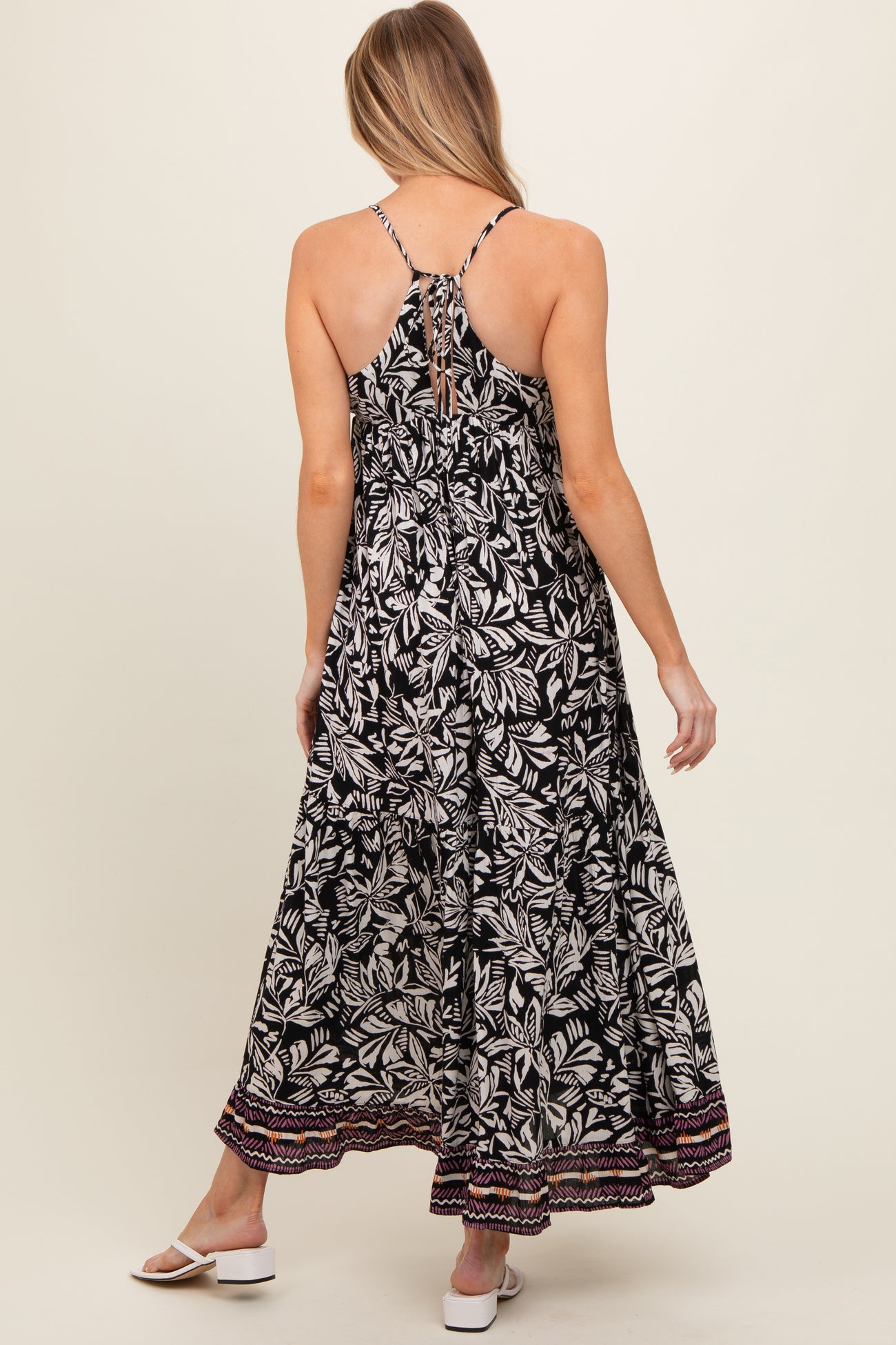 woman wearing a black and white floral print maternity maxi dress with a tie back and colorful hem detail