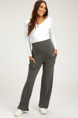 woman wearing a white long sleeve maternity top and grey maternity pants with pockets, smiling and standing confidently