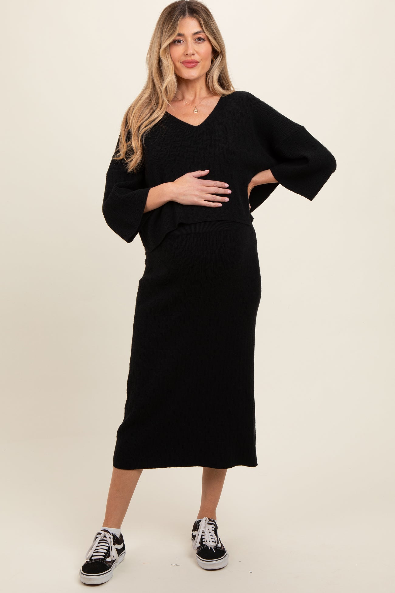 woman wearing a black maternity two-piece outfit with a v-neck top and a midi skirt, holding her baby bump