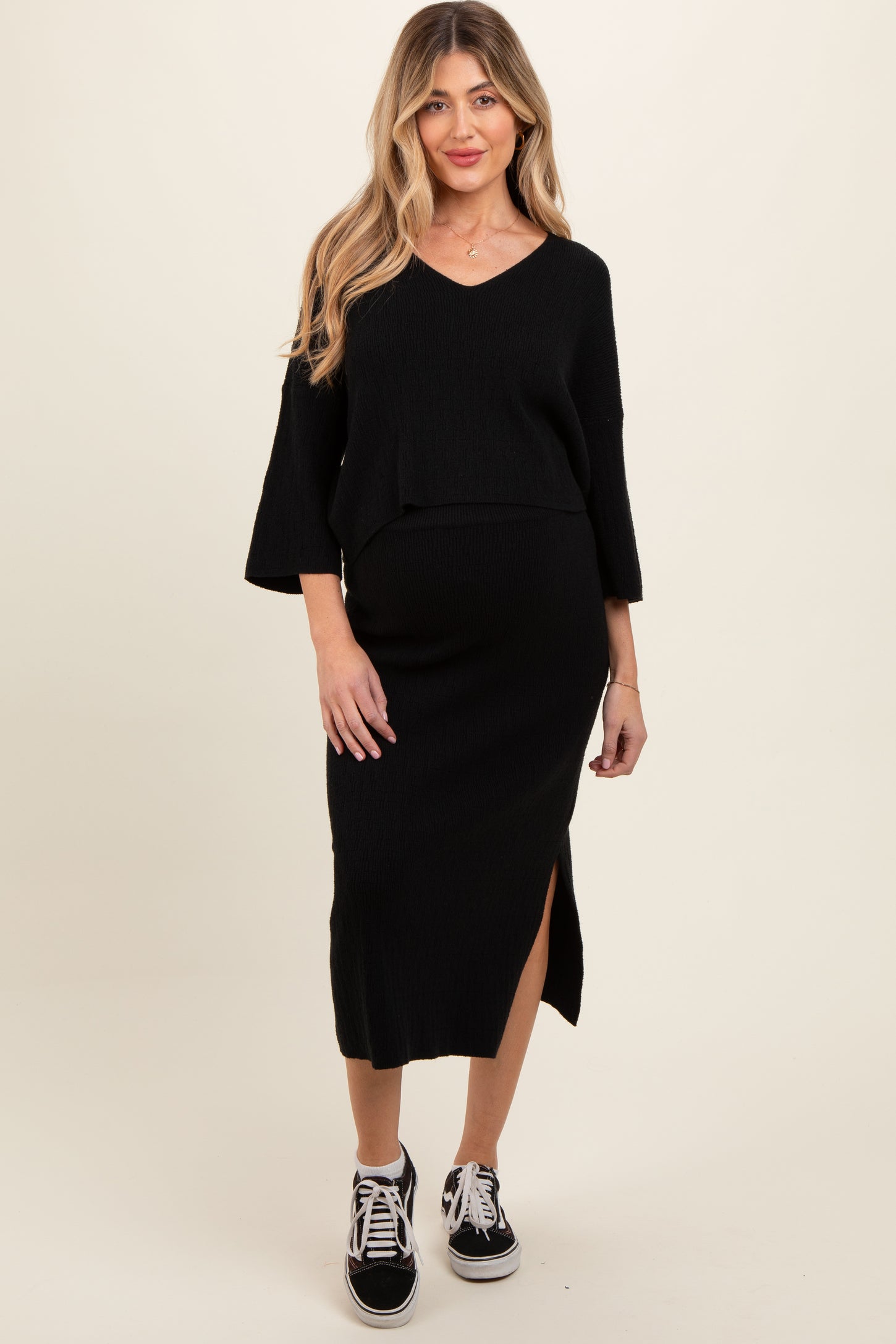 woman wearing a black maternity two-piece outfit with a v-neck top and a midi skirt featuring a side slit