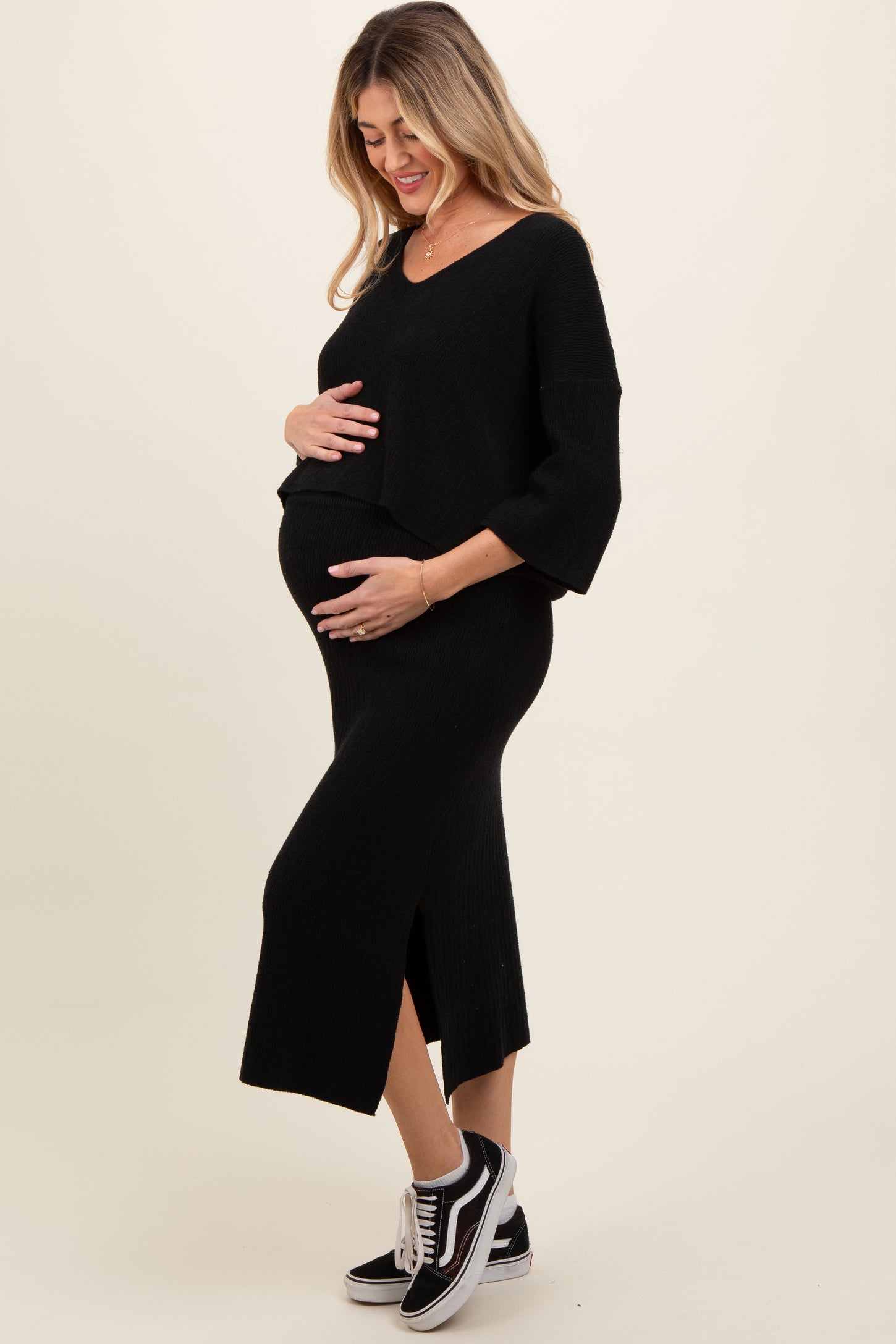woman wearing a black maternity dress with a side slit and oversized sleeves, holding her baby bump