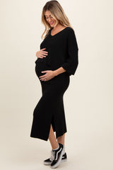 woman wearing a black maternity dress with a side slit and oversized sleeves, holding her baby bump