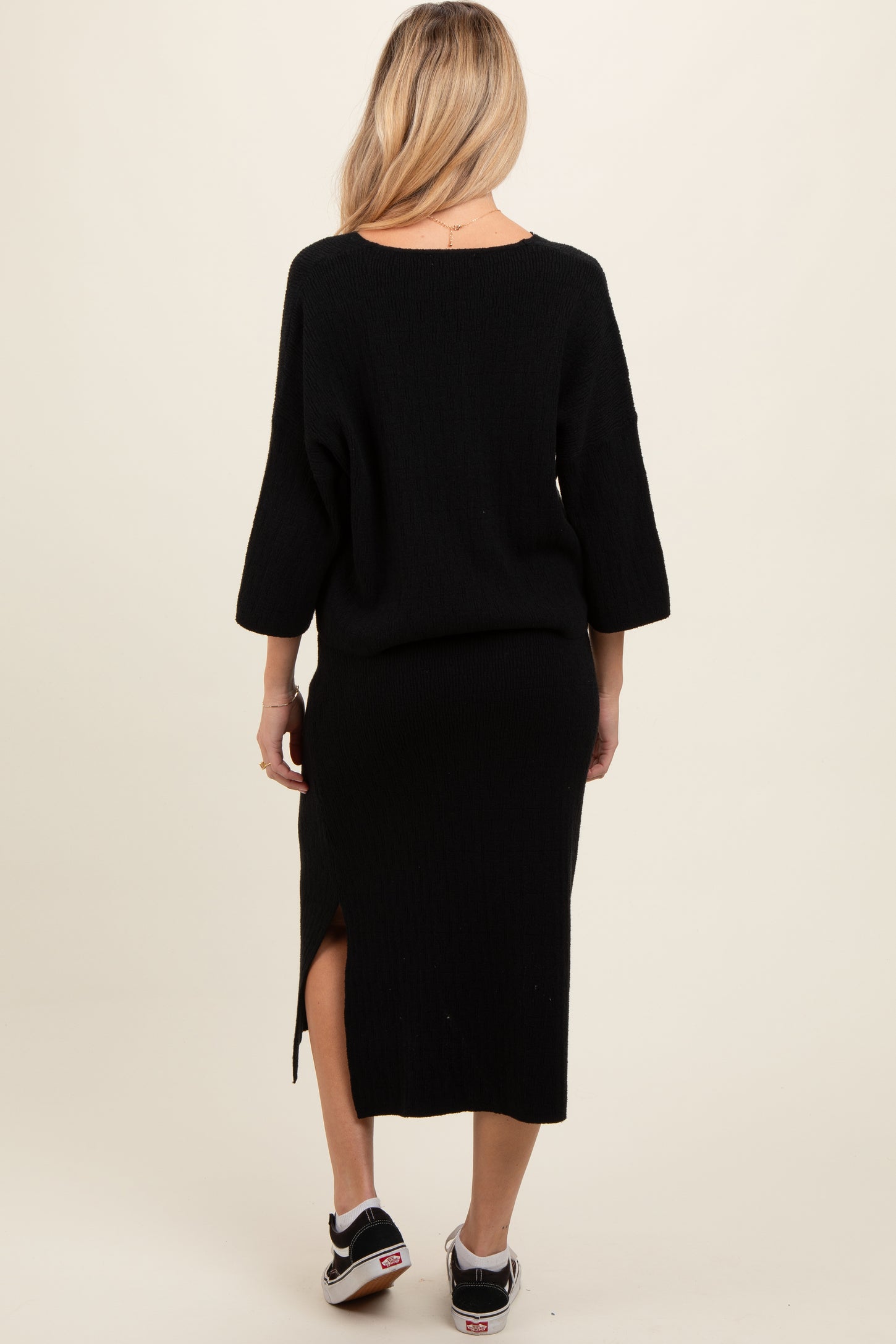 woman wearing a black maternity knit dress with a side slit and three-quarter sleeves, viewed from the back
