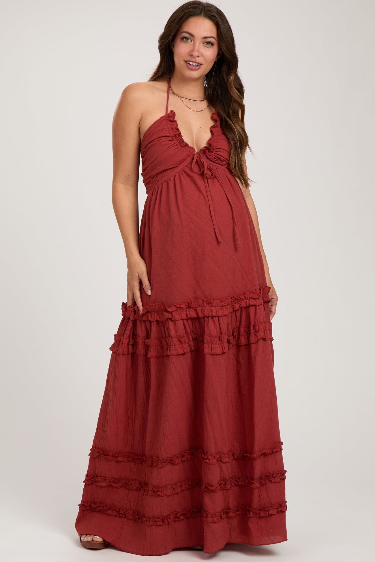 woman wearing a rust red maternity maxi dress with ruffle details and a halter neckline, showcasing her baby bump