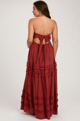 woman wearing a rust-colored strapless maternity maxi dress with a tied back and ruffle details