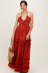 woman wearing a rust red halter maxi dress with ruffle details, holding a woven bag