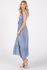woman wearing a light blue smocked maxi dress with flutter sleeves and a tiered skirt, standing in profile