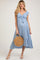 woman wearing a light blue maternity dress with tie front detail and flutter sleeves, holding a woven bag, and showcasing her baby bump