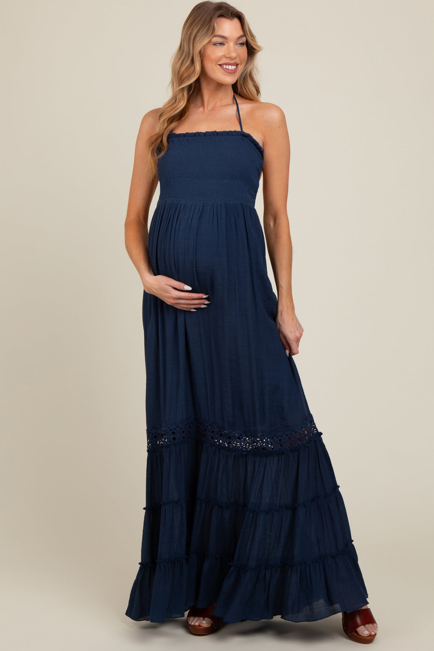 woman wearing a navy blue maternity maxi dress with a smocked bodice and tiered ruffle hem, gently cradling her baby bump