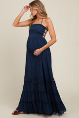woman wearing a navy blue maternity maxi dress with a smocked bodice and tiered ruffle hem, holding her baby bump