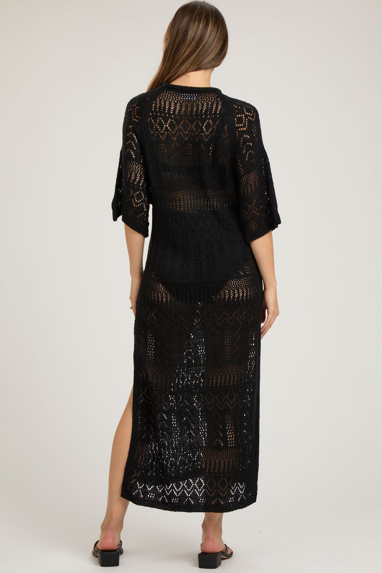 woman wearing a black open-knit maternity cover-up dress with three-quarter sleeves and side slits