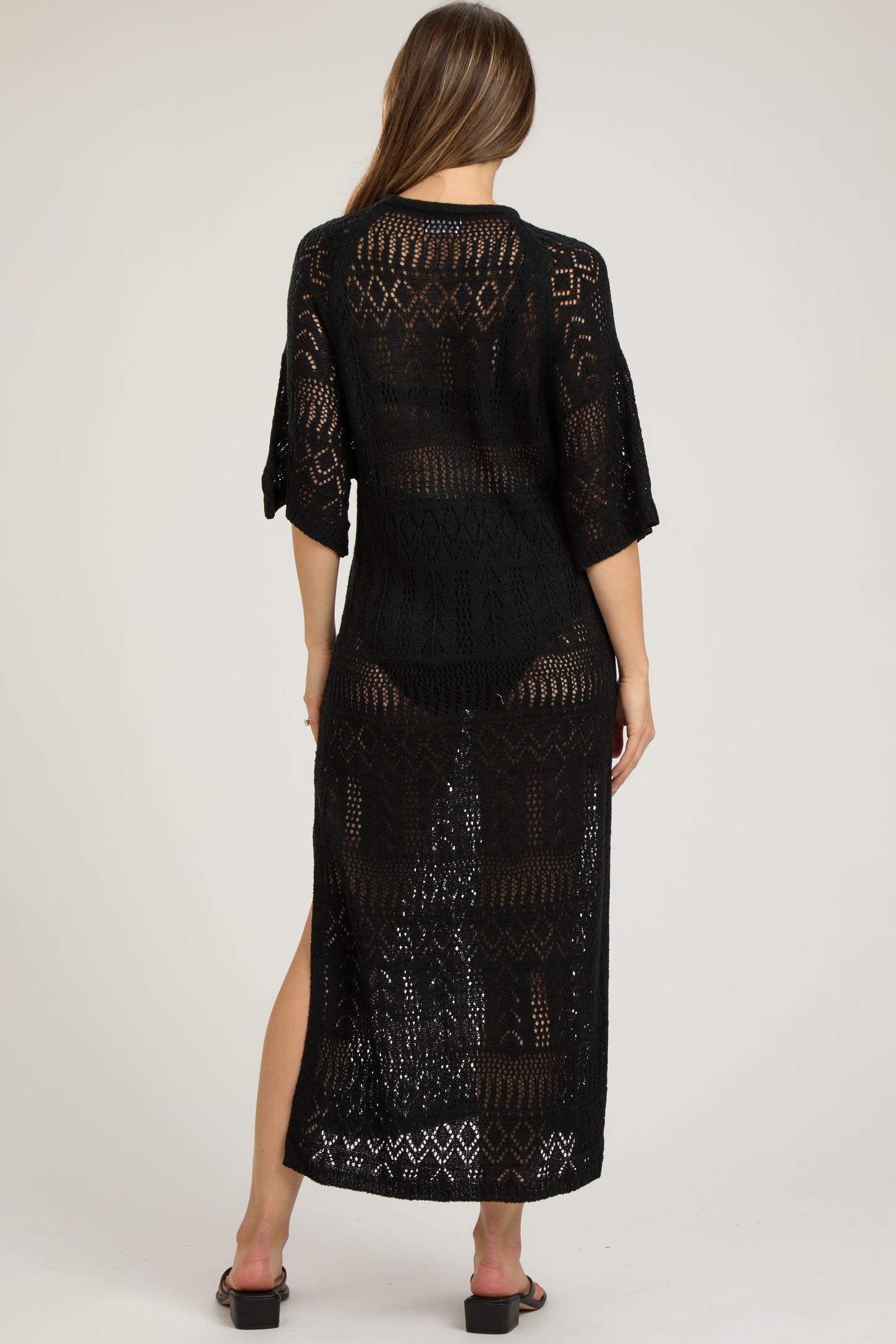 woman wearing a black open-knit maternity cover-up dress with three-quarter sleeves and side slits