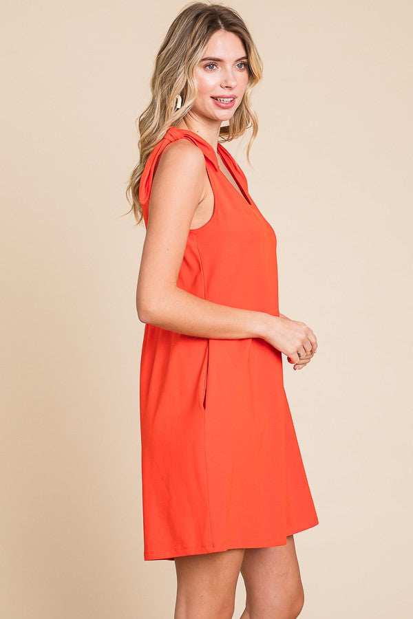 woman wearing an orange sleeveless dress with tie details on the shoulders and a relaxed fit