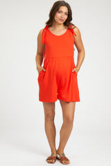 woman wearing a bright red maternity romper with shoulder ties and pockets, showcasing her baby bump