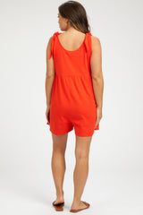 woman wearing a bright orange maternity romper with tie straps, showing a relaxed fit and gathered waist.