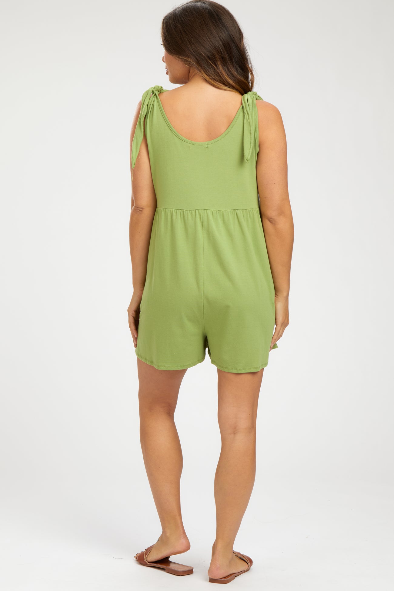 woman wearing a green maternity romper with tie straps and a relaxed fit, seen from the back