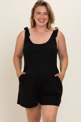 woman wearing a black maternity plus romper with shoulder ties and pockets, smiling at the camera