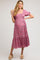 woman wearing a pink floral maternity dress with short puff sleeves and a smocked bodice, posing with a relaxed smile