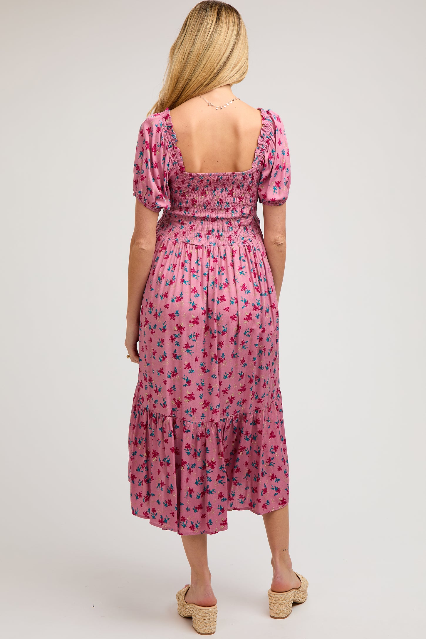 woman wearing a floral pink maternity midi dress with a smocked bodice and puff sleeves, showing her back