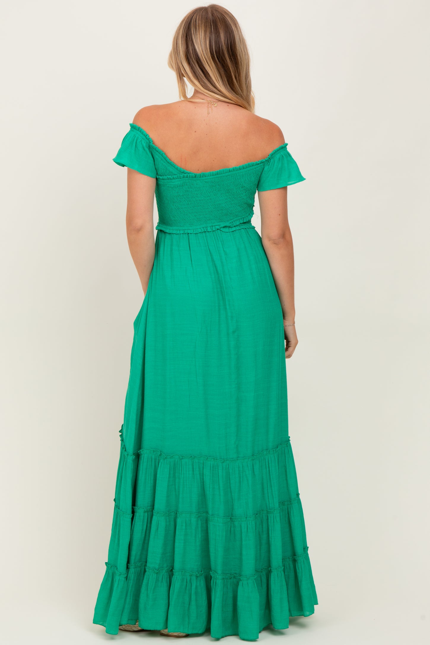 woman wearing a green off-the-shoulder maxi dress with a tiered skirt and a fitted bodice