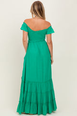 woman wearing a green off-the-shoulder maxi dress with a tiered skirt and a fitted bodice