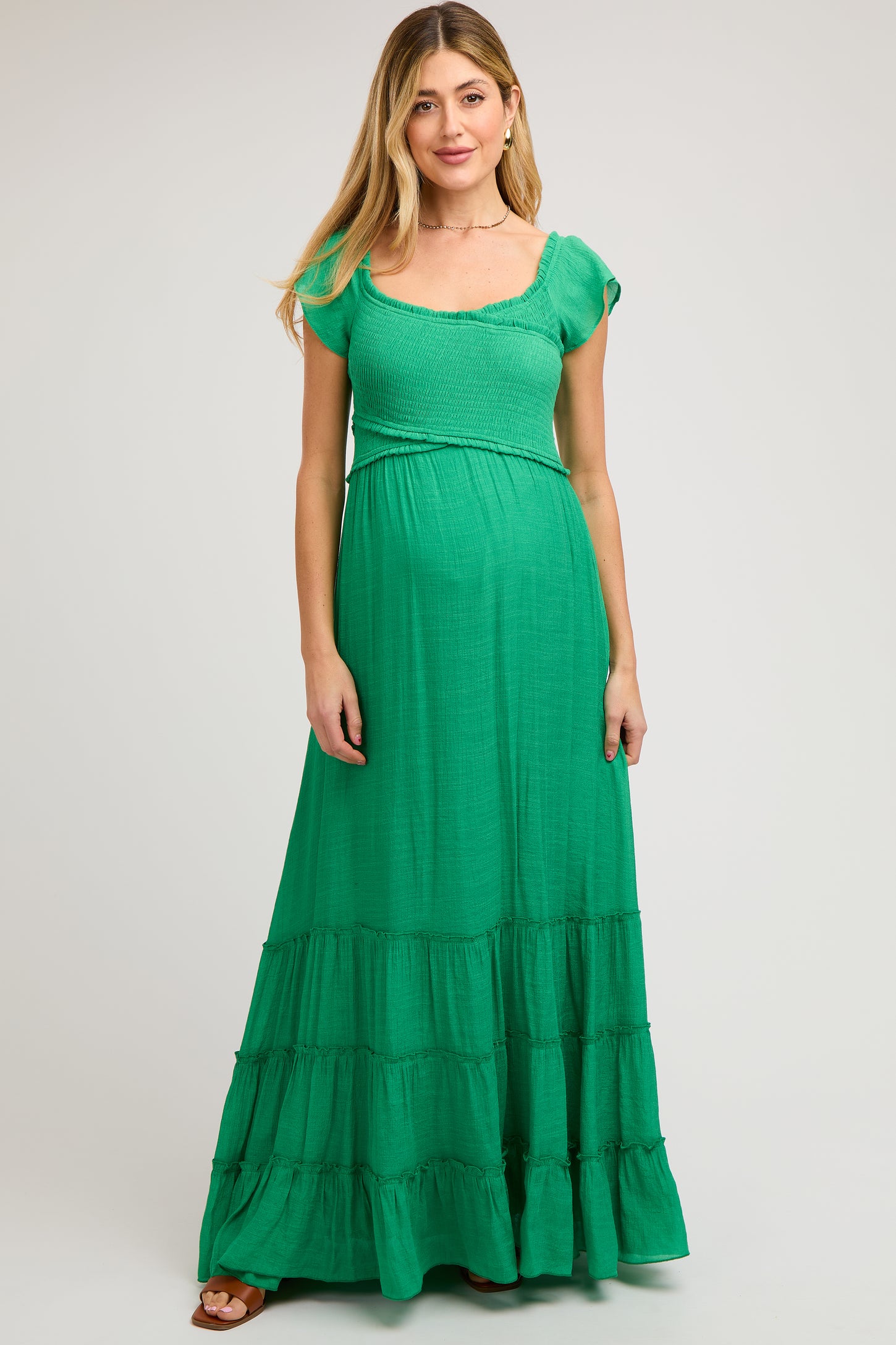 woman wearing a green maxi maternity dress with short sleeves and tiered skirt, showcasing a baby bump