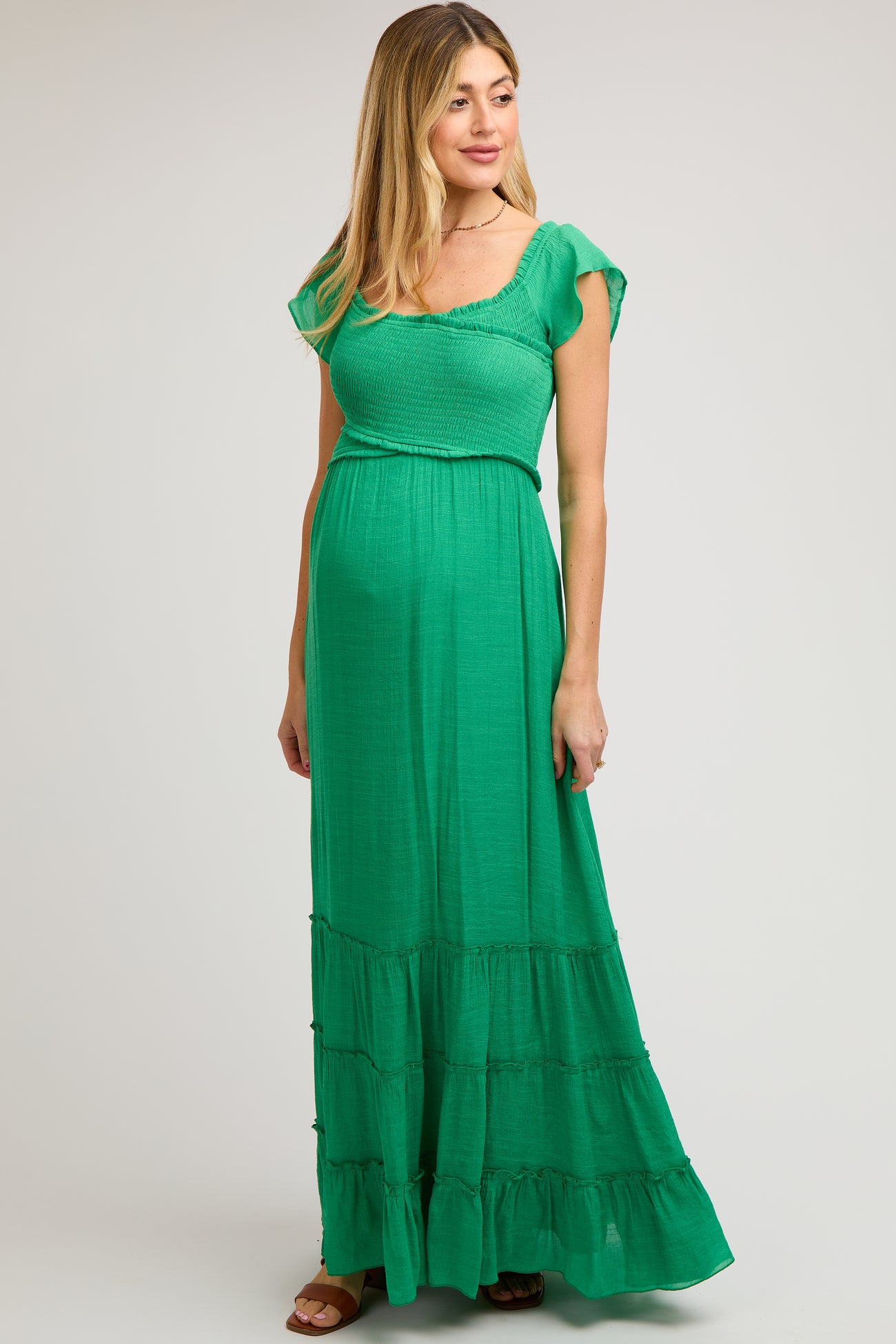 woman wearing a green maternity maxi dress with a smocked bodice and tiered ruffle hem, showing her baby bump