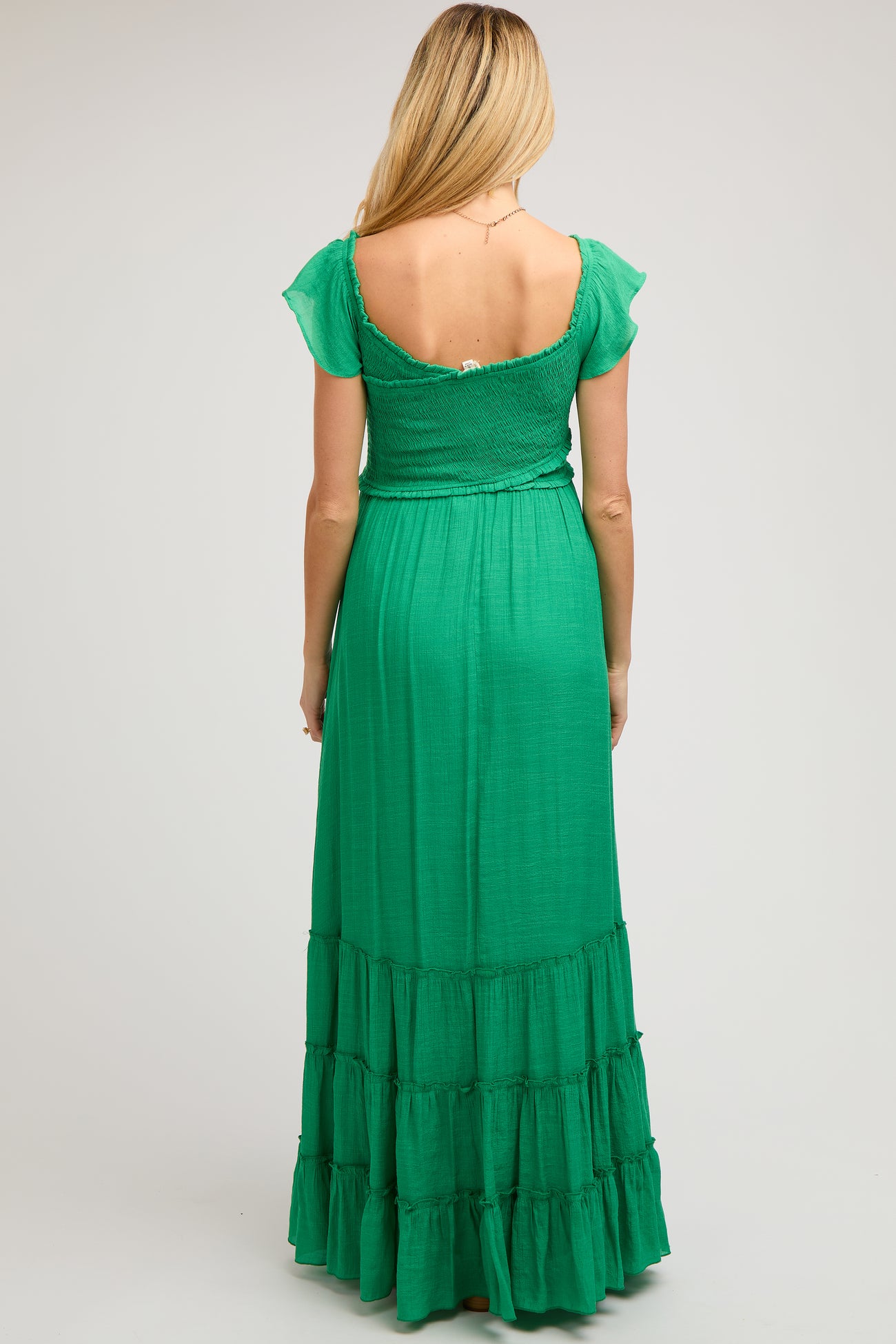 woman wearing a green maternity maxi dress with flutter sleeves and a tiered skirt, showing the back view