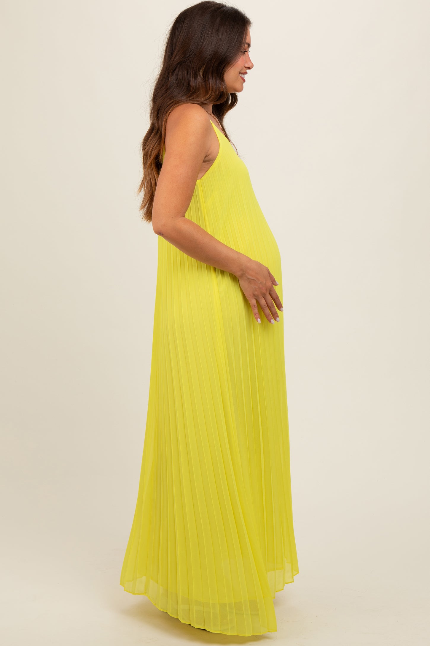 woman wearing a bright yellow pleated maternity maxi dress and showcasing her baby bump
