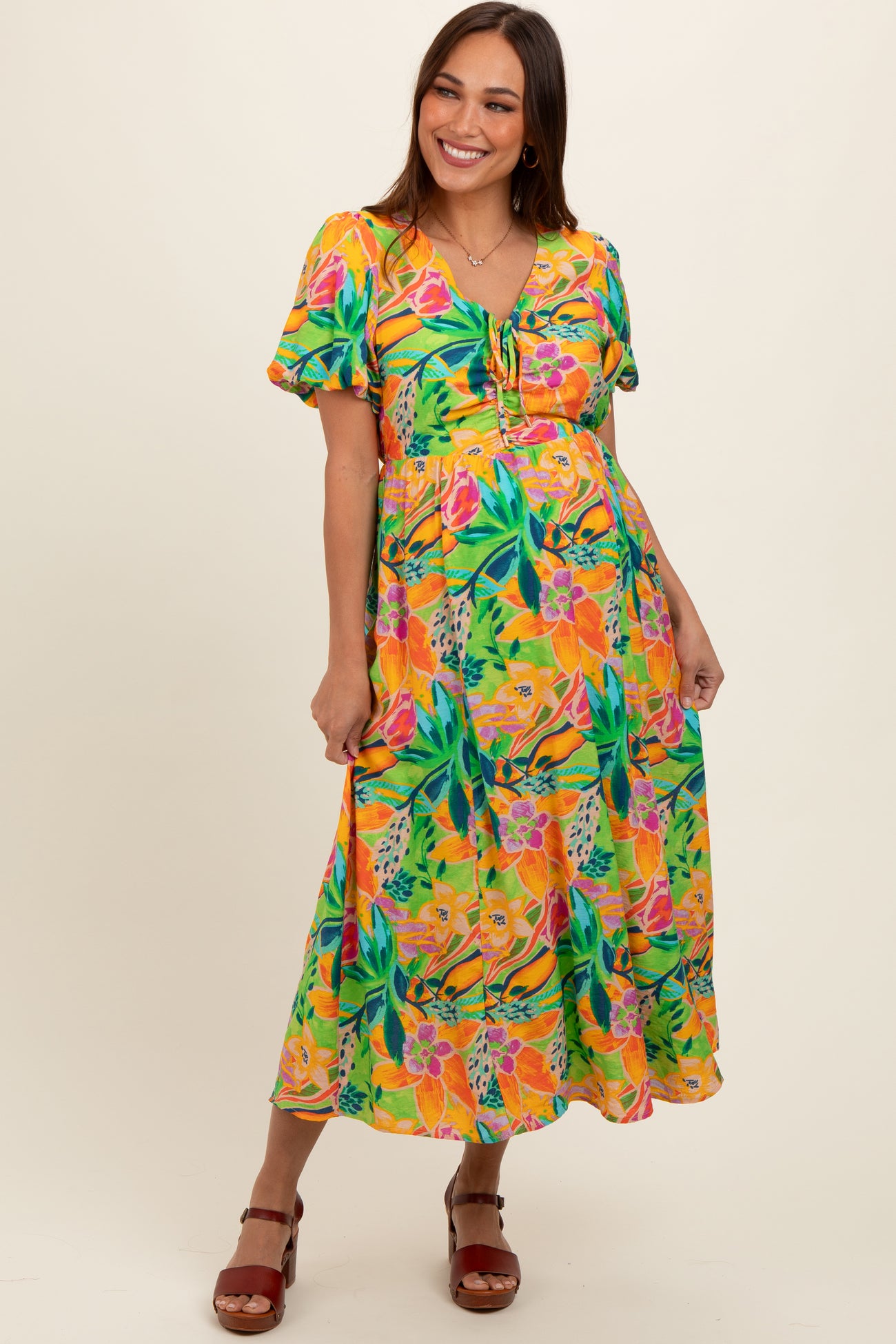 woman wearing a vibrant floral maternity dress with short sleeves and a tie detail, showcasing her baby bump