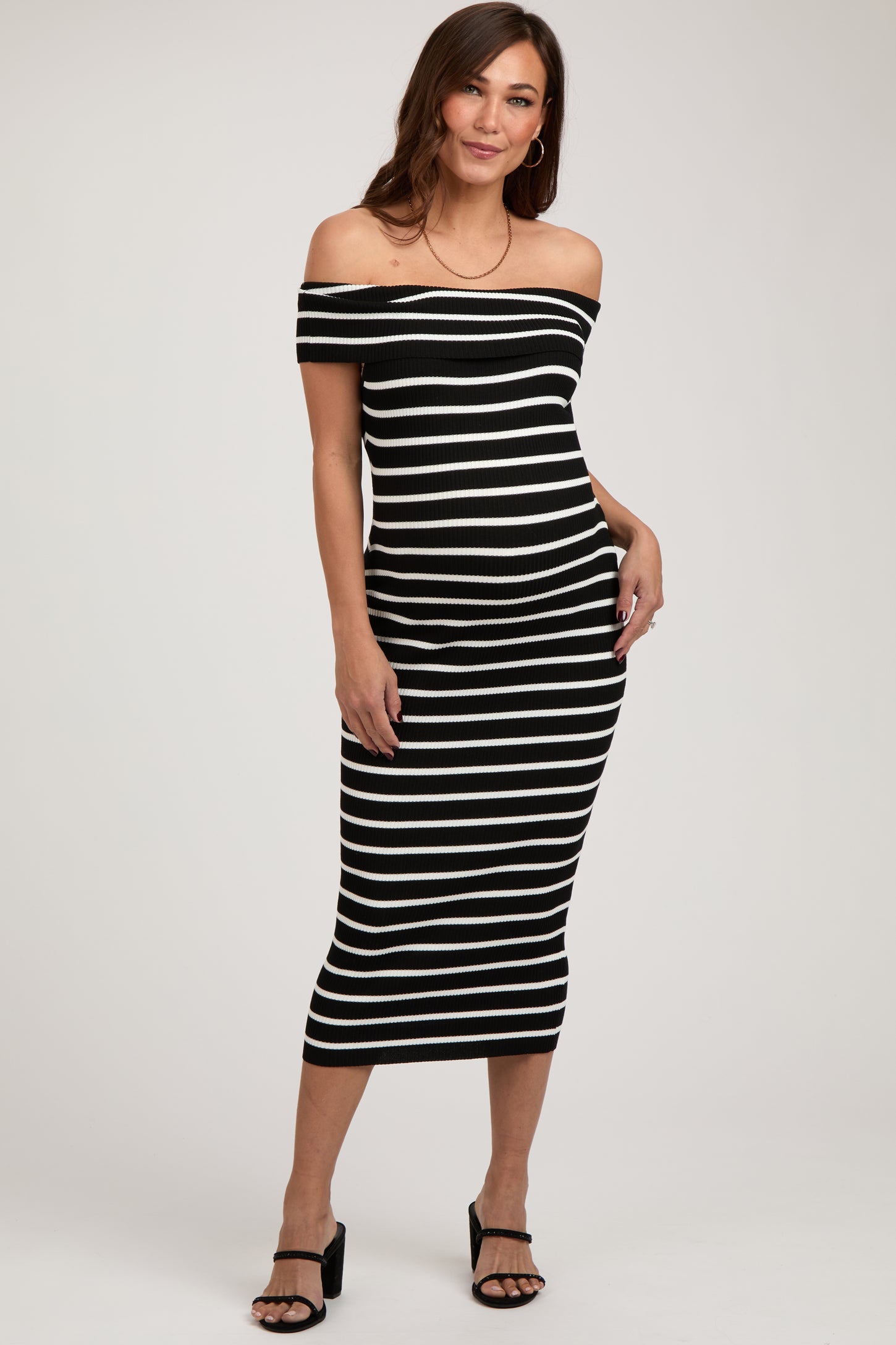 woman wearing a black and white striped off-the-shoulder maternity dress fitted to highlight her baby bump