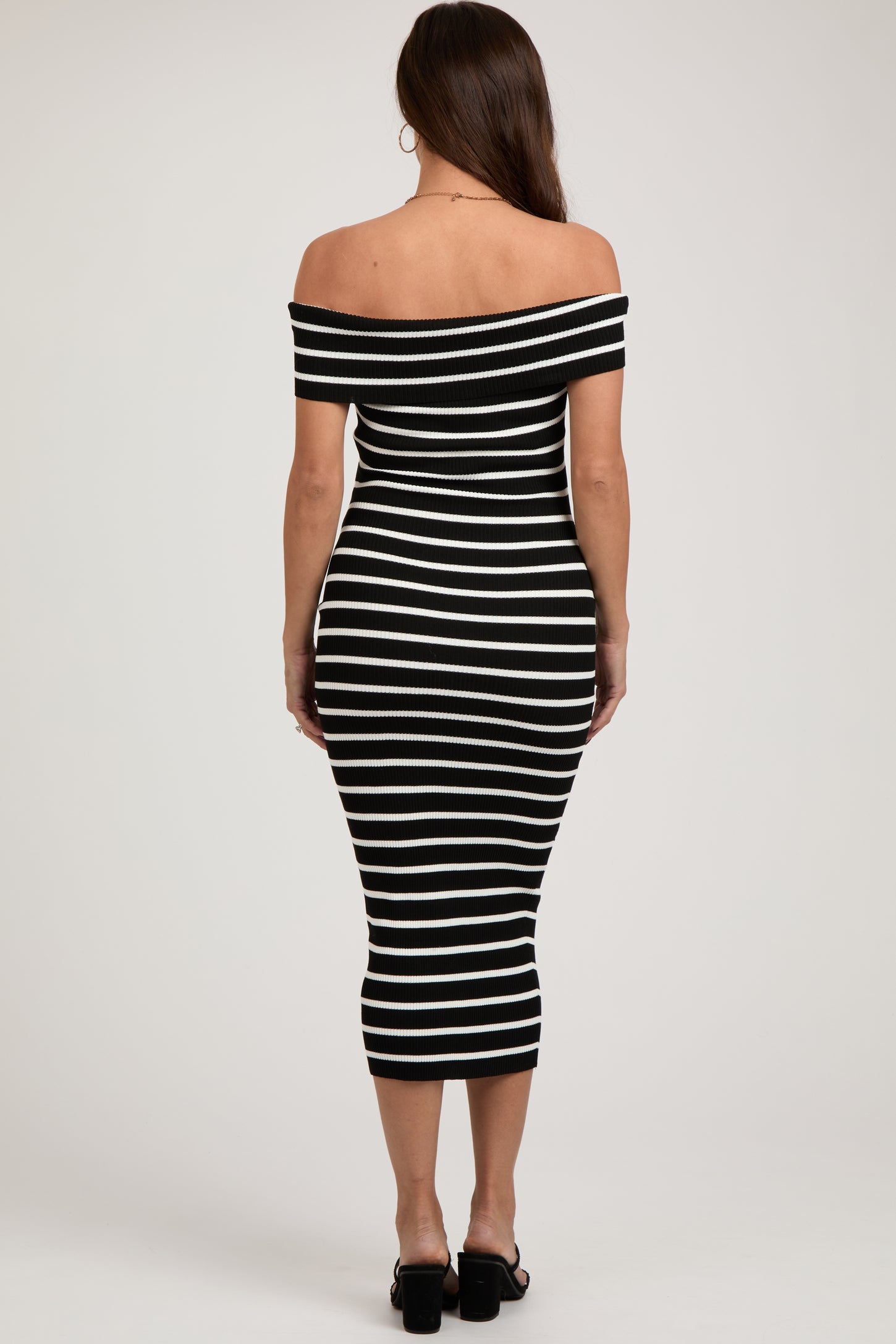 woman wearing a black and white striped off-the-shoulder maternity dress, fitted style, showing her back