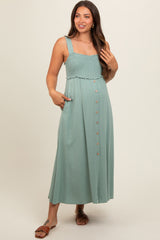 woman wearing a teal maternity maxi dress with smocked bodice and button-down front, posing with one hand on her hip