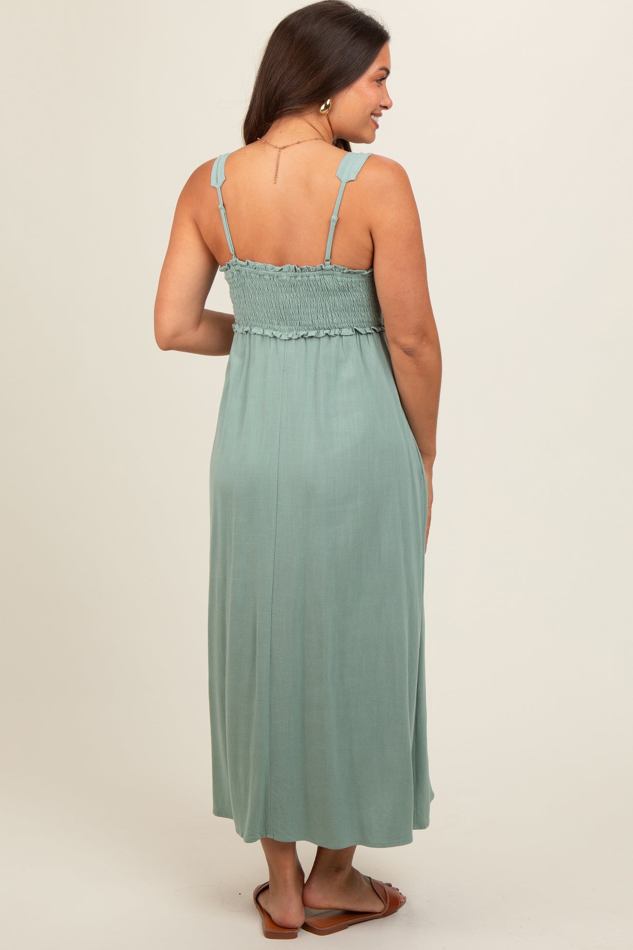 woman wearing a sage green maternity maxi dress with a smocked bodice and adjustable straps from the back