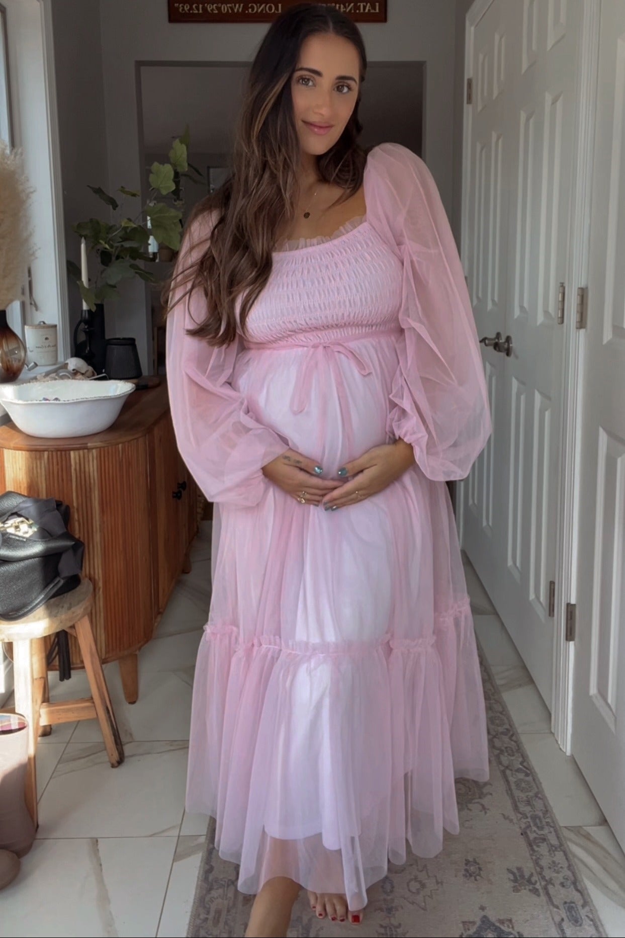 woman wearing a pink maternity dress with puff sleeves and a tiered skirt, highlighting her baby bump