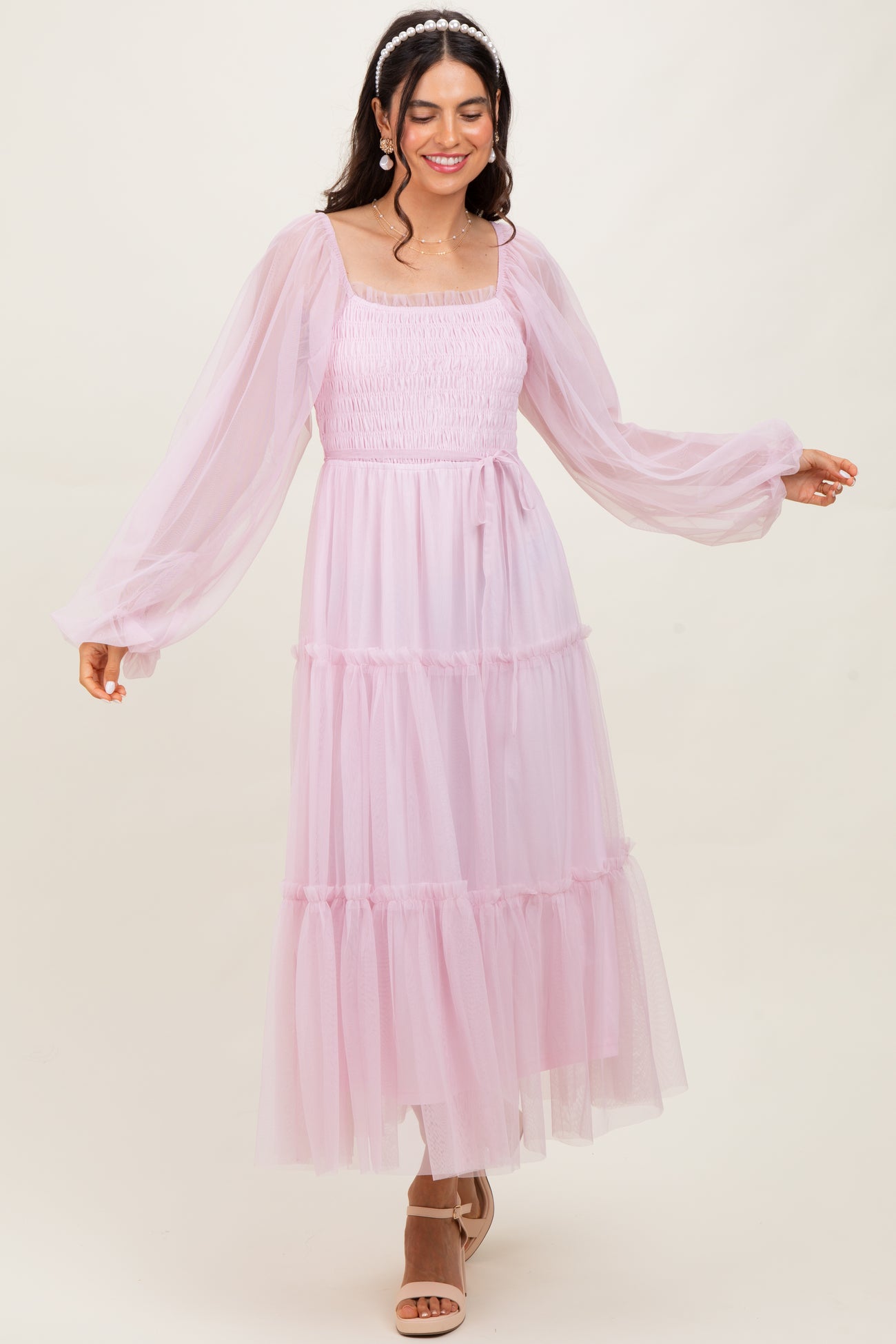 woman wearing a light pink tiered tulle maxi dress with long sleeves and a square neckline