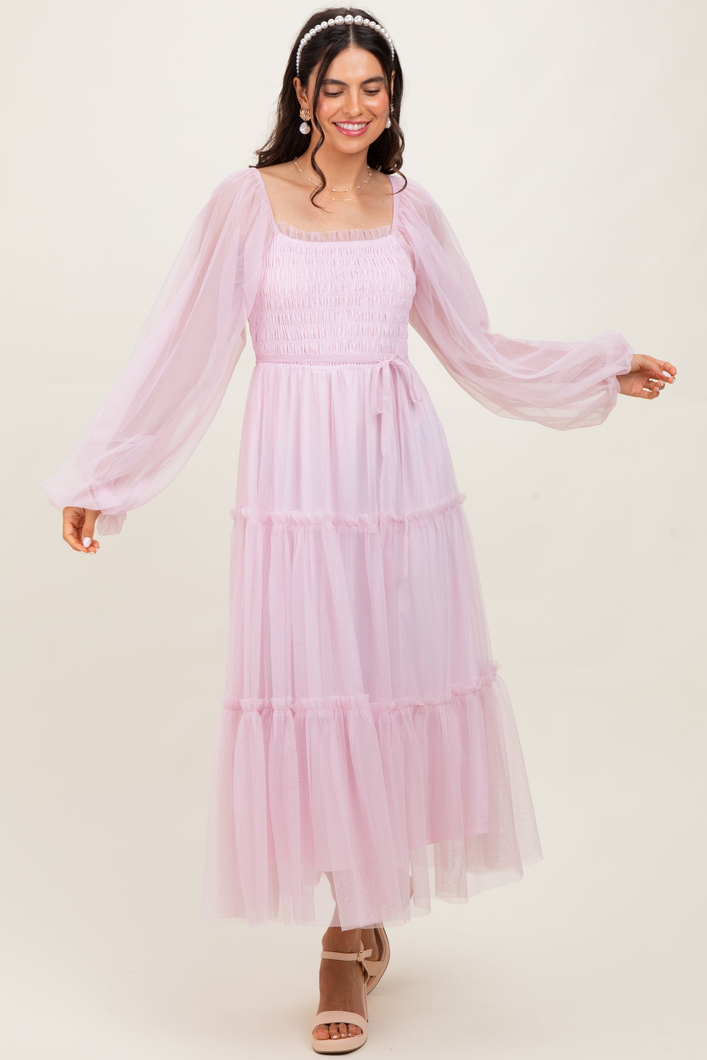 woman wearing a light pink tiered tulle maxi dress with long sleeves and a square neckline