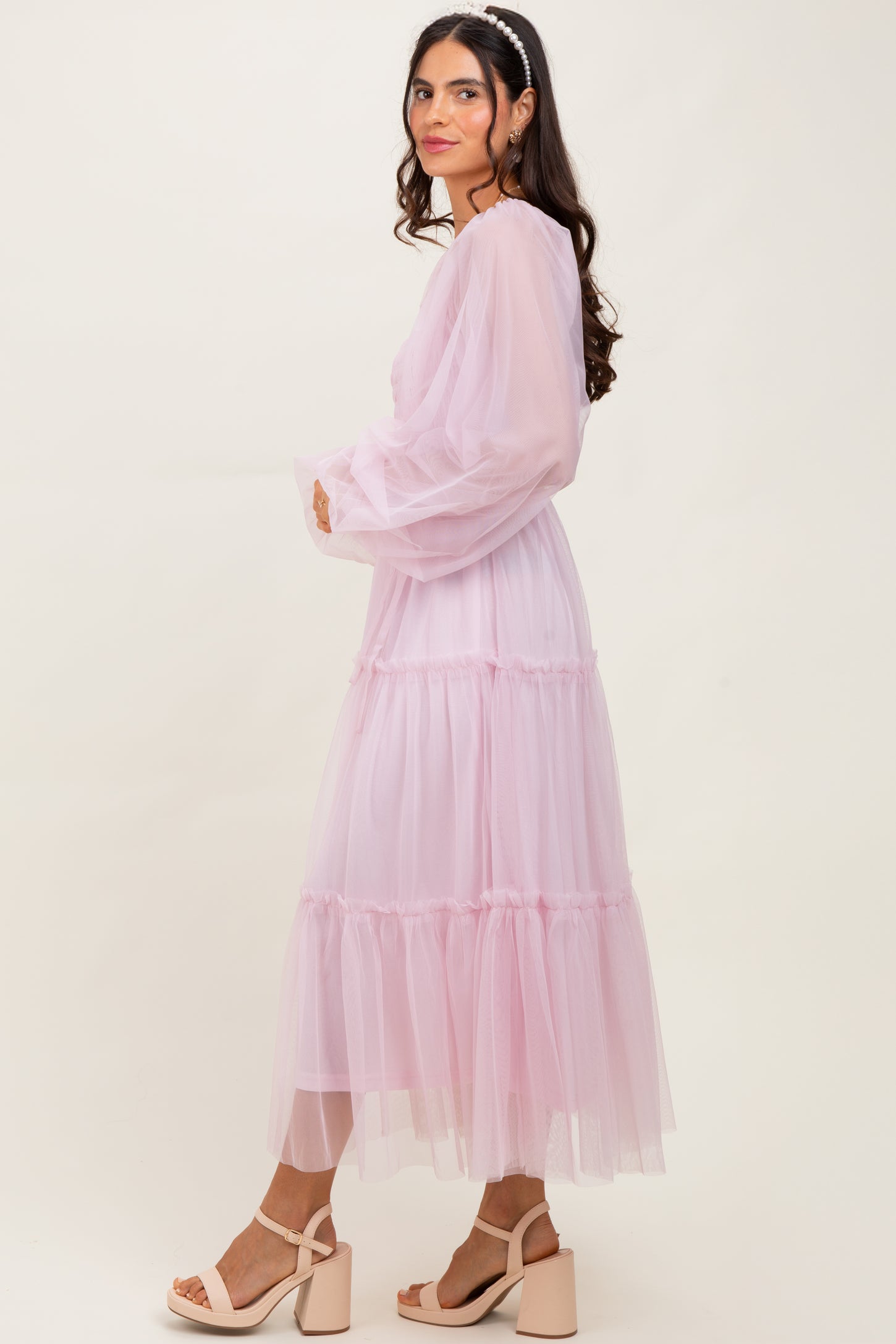 woman wearing a flowy pink midi dress with tiered tulle layers and long sheer sleeves