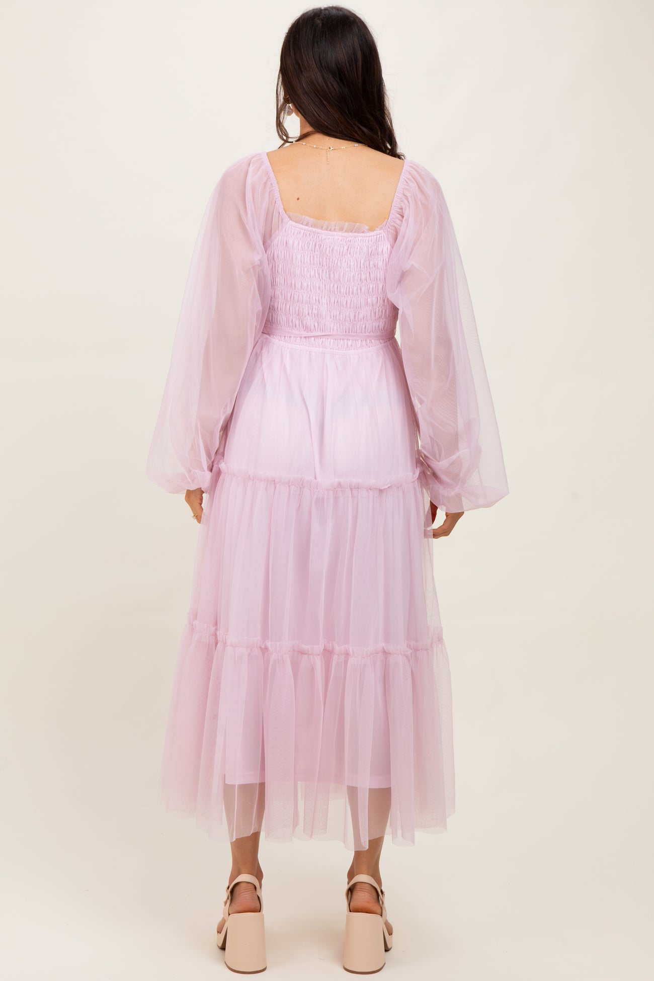 woman wearing a long pastel pink tulle dress with puff sleeves and tiered ruffles, viewed from the back