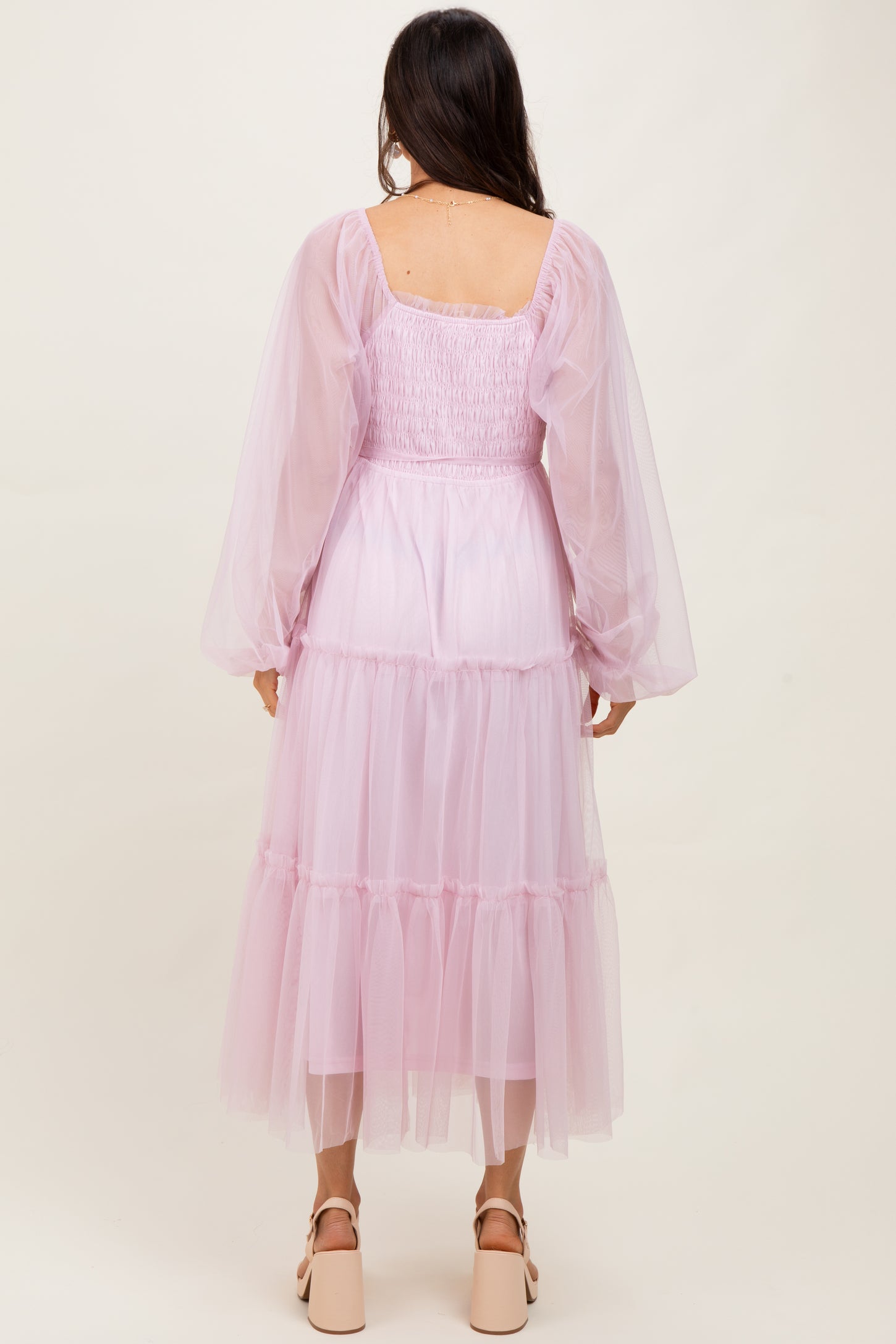 woman wearing a long pastel pink tulle dress with puff sleeves and tiered ruffles, viewed from the back
