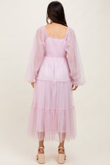 woman wearing a long pastel pink tulle dress with puff sleeves and tiered ruffles, viewed from the back