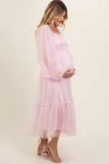 woman wearing a pink maternity dress with puff sleeves and tiered skirt, holding her baby bump